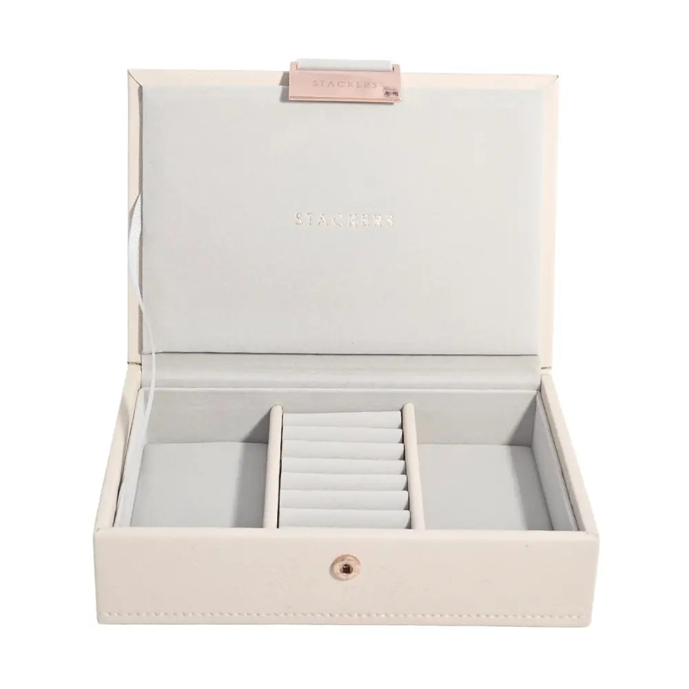 An open rectangular jewelry box in a light cream color with a pale gray velvet interior. The box is divided into two sections, with one section featuring a central roll organizer.